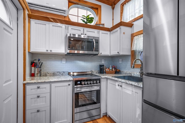 kitchen featuring white cabinets, stainless steel appliances, a wall unit AC, and sink