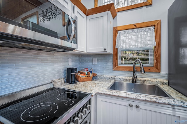 kitchen featuring light stone countertops, backsplash, stainless steel appliances, sink, and white cabinetry