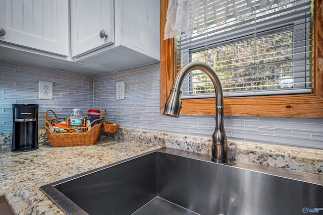 interior details with decorative backsplash, white cabinetry, light stone countertops, and sink