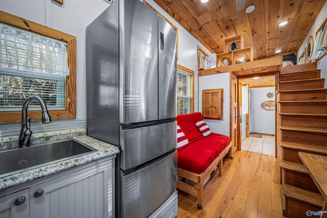 kitchen with wooden ceiling, sink, light stone countertops, light hardwood / wood-style floors, and stainless steel refrigerator