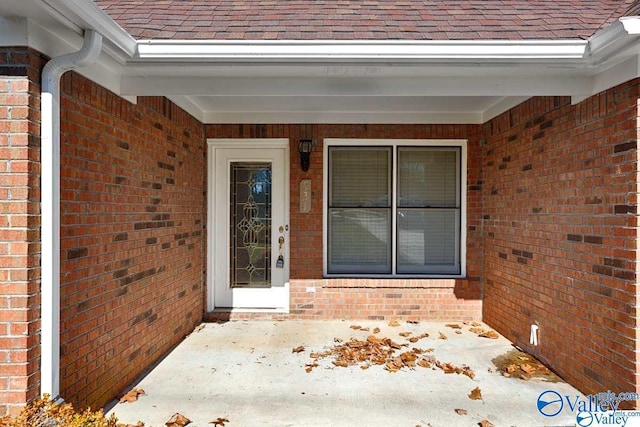 doorway to property featuring a shingled roof and brick siding