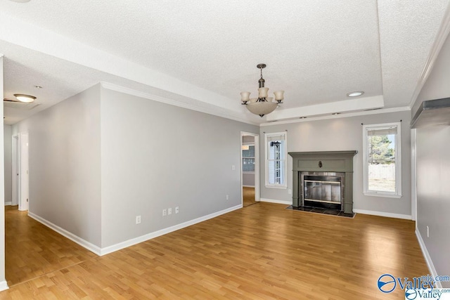 unfurnished living room featuring a tray ceiling, a notable chandelier, light wood finished floors, a fireplace with flush hearth, and a textured ceiling