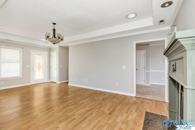 unfurnished living room with a chandelier, a fireplace with flush hearth, visible vents, light wood-style floors, and a raised ceiling