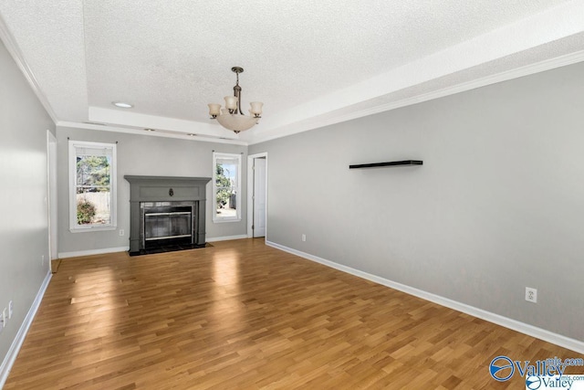 unfurnished living room featuring light wood-type flooring, a tray ceiling, a textured ceiling, and baseboards