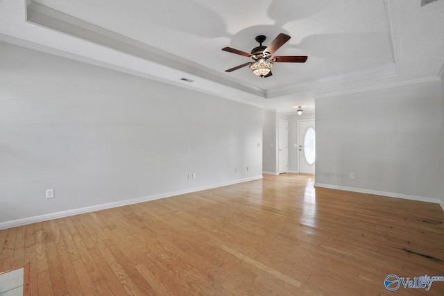 spare room featuring light wood-type flooring, a raised ceiling, ceiling fan, and crown molding