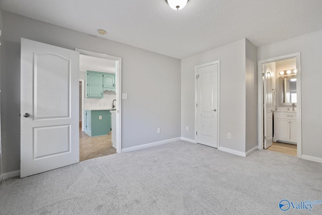 unfurnished bedroom with light carpet, a textured ceiling, ensuite bathroom, and sink