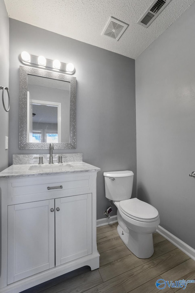 bathroom with hardwood / wood-style floors, vanity, a textured ceiling, and toilet