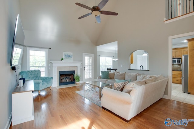 living room with ceiling fan, high vaulted ceiling, a tile fireplace, light wood-type flooring, and crown molding