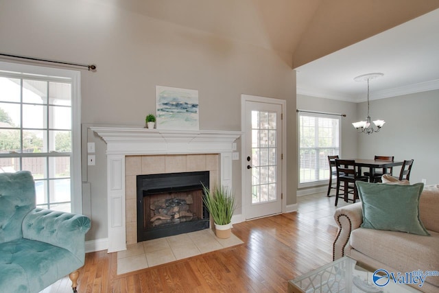 living room featuring vaulted ceiling, a tiled fireplace, light wood-type flooring, an inviting chandelier, and ornamental molding