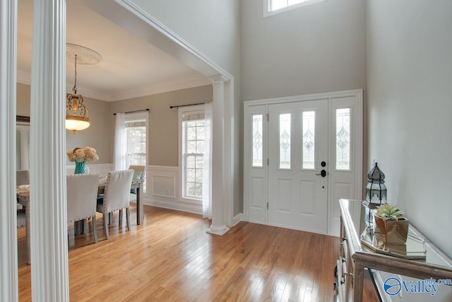 foyer entrance featuring ornamental molding, light wood-type flooring, decorative columns, and a healthy amount of sunlight