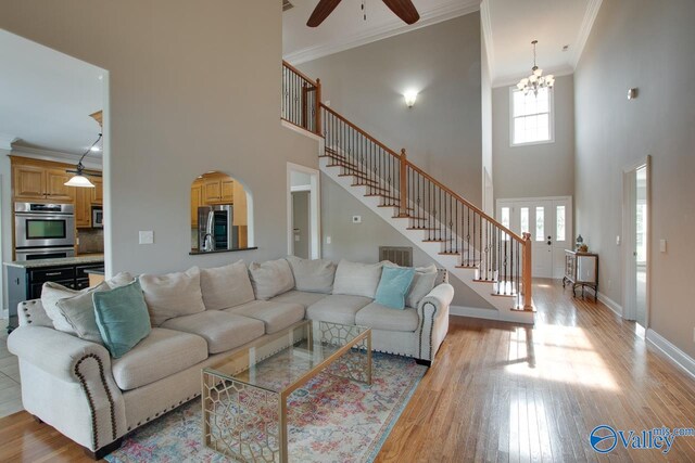 living room featuring ceiling fan with notable chandelier, a towering ceiling, crown molding, and light hardwood / wood-style flooring