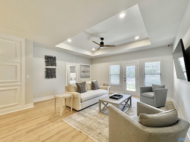 living room with light wood-type flooring, a tray ceiling, and ceiling fan