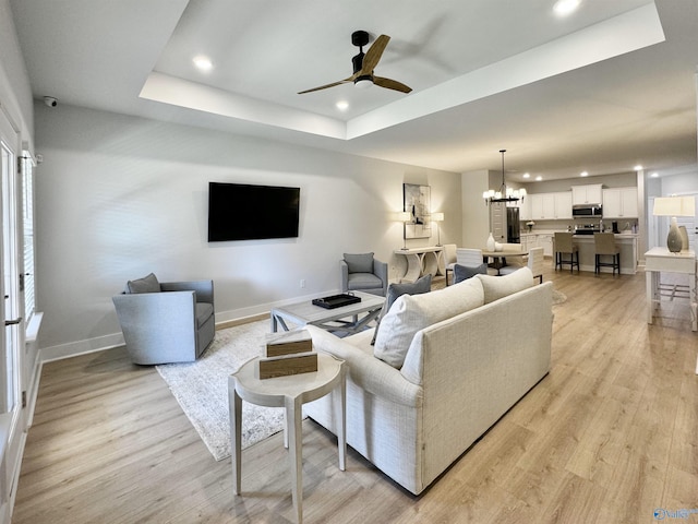 living room featuring ceiling fan with notable chandelier, a raised ceiling, and light hardwood / wood-style flooring