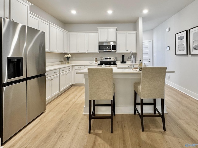 kitchen featuring stainless steel appliances, sink, an island with sink, white cabinets, and light hardwood / wood-style flooring