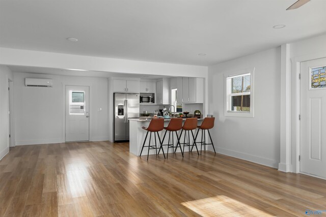 kitchen with a breakfast bar area, a wall mounted AC, a wealth of natural light, and stainless steel appliances