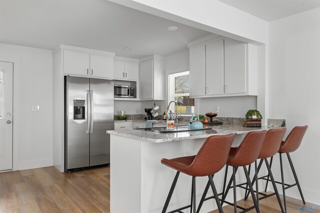 kitchen featuring kitchen peninsula, appliances with stainless steel finishes, a breakfast bar, white cabinets, and light hardwood / wood-style floors