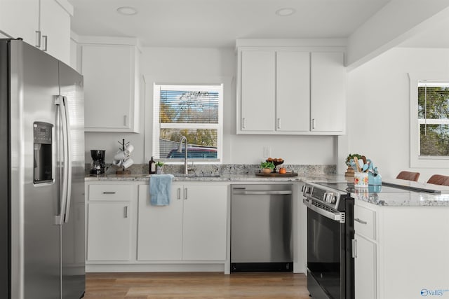 kitchen featuring light wood-type flooring, light stone counters, stainless steel appliances, sink, and white cabinets