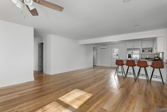 living room featuring a wall mounted AC, light wood-type flooring, and ceiling fan