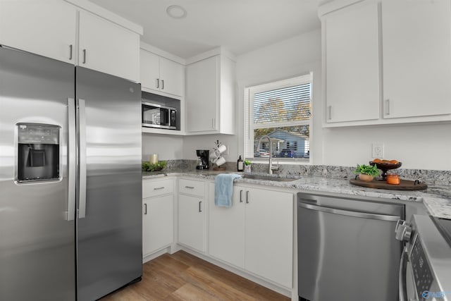 kitchen featuring light stone countertops, white cabinetry, sink, stainless steel appliances, and light wood-type flooring