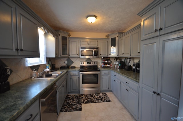 kitchen featuring decorative backsplash, glass insert cabinets, appliances with stainless steel finishes, gray cabinetry, and a sink