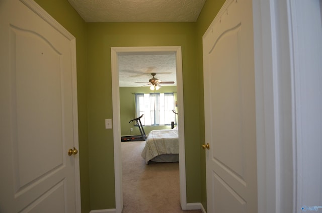 corridor featuring a textured ceiling, carpet floors, and baseboards