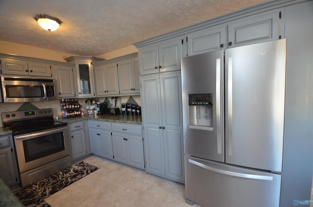 kitchen featuring stainless steel appliances, gray cabinets, glass insert cabinets, and a textured ceiling