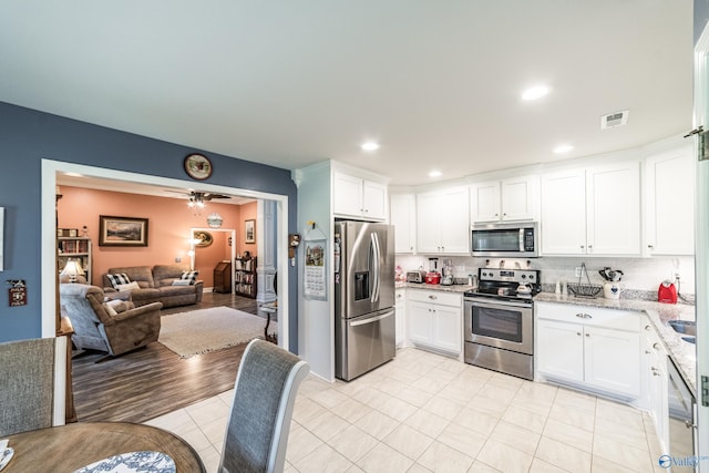kitchen featuring visible vents, tasteful backsplash, white cabinets, open floor plan, and stainless steel appliances