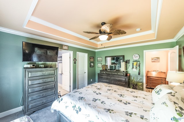 carpeted bedroom with ensuite bathroom, ornamental molding, a ceiling fan, and a tray ceiling