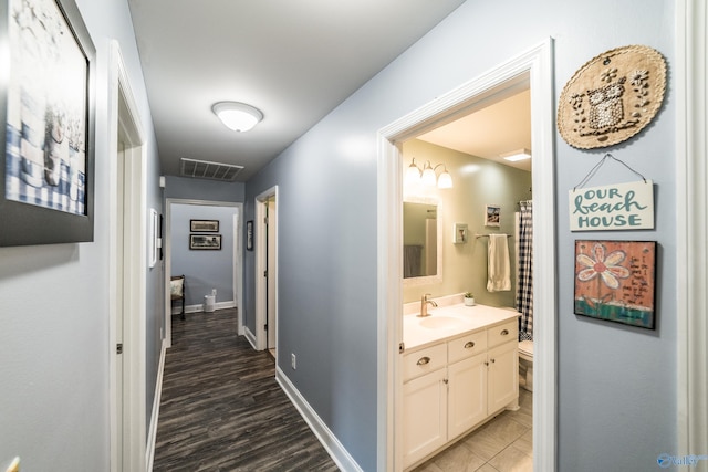 corridor featuring a sink, baseboards, wood finished floors, and visible vents