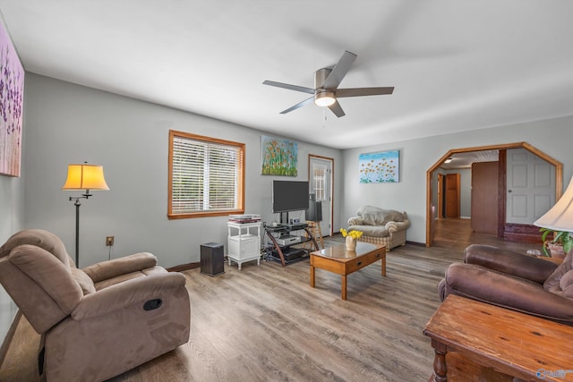 living room featuring a ceiling fan, arched walkways, baseboards, and wood finished floors