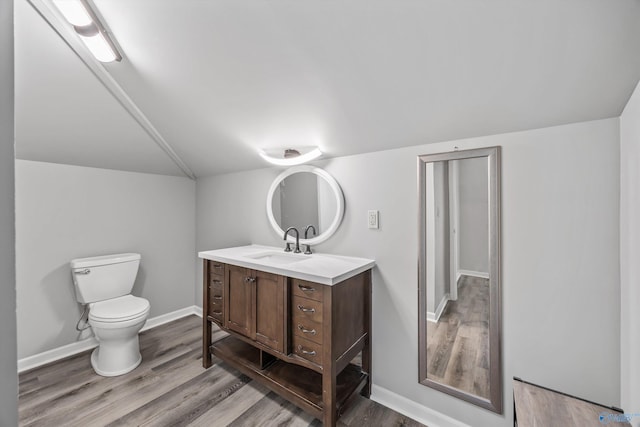 bathroom featuring toilet, wood finished floors, vanity, baseboards, and vaulted ceiling