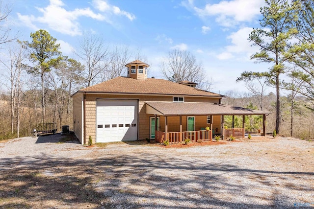 view of front of property with a garage, covered porch, dirt driveway, and cooling unit