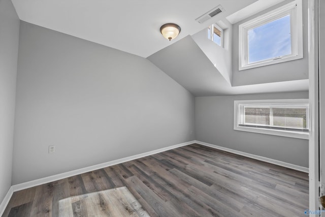 additional living space with baseboards, visible vents, vaulted ceiling, and wood finished floors