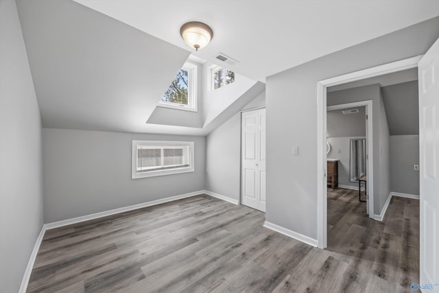 additional living space with lofted ceiling, wood finished floors, visible vents, and baseboards