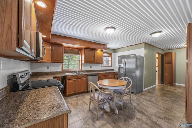 kitchen with baseboards, appliances with stainless steel finishes, brown cabinets, a sink, and backsplash