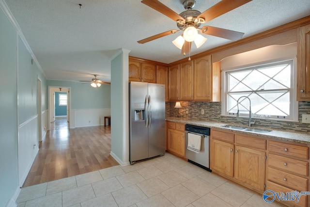 kitchen featuring light stone countertops, a sink, appliances with stainless steel finishes, decorative backsplash, and crown molding