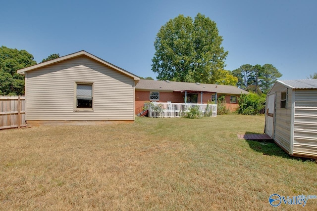 back of house with fence, a storage unit, a lawn, and an outbuilding