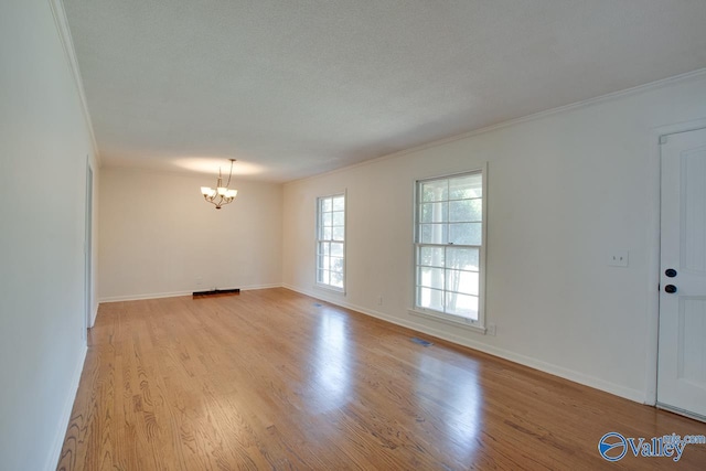 spare room with light wood-style floors, a notable chandelier, ornamental molding, and baseboards