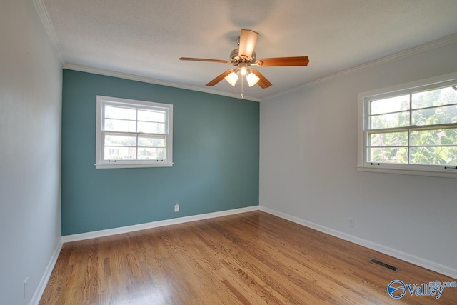 unfurnished room with ceiling fan, light wood-style flooring, visible vents, baseboards, and ornamental molding