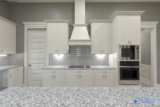 kitchen with custom exhaust hood, white cabinetry, black electric stovetop, and light stone counters