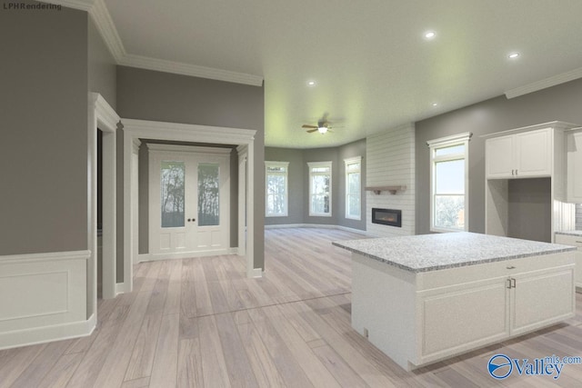 kitchen with white cabinetry, a center island, ornamental molding, a large fireplace, and light wood-type flooring