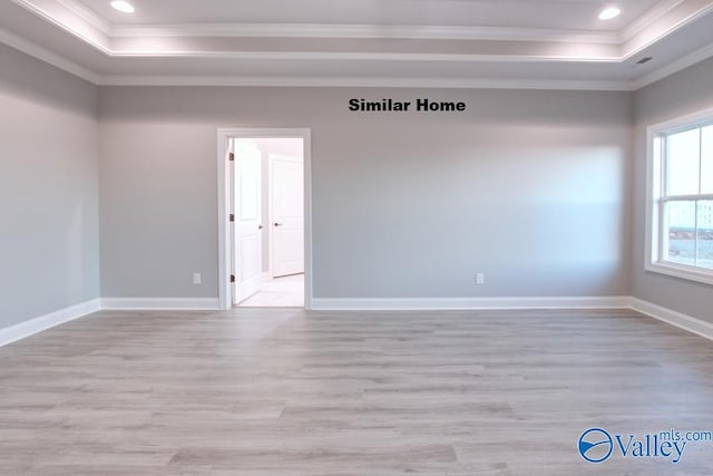 unfurnished room featuring a tray ceiling, ornamental molding, and light wood-type flooring