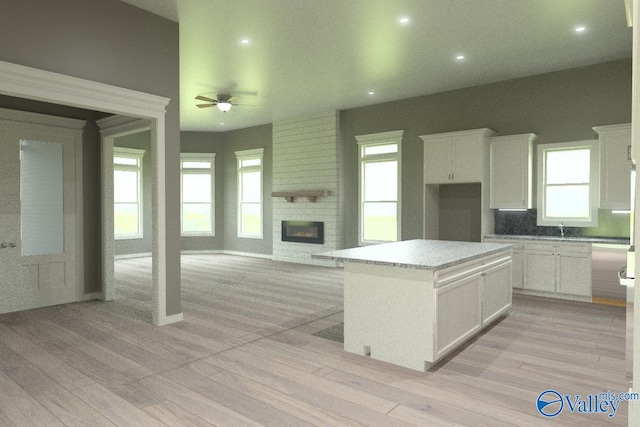 kitchen with white cabinetry, a kitchen island, a large fireplace, and a wealth of natural light