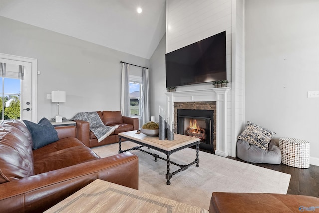 living area featuring baseboards, recessed lighting, wood finished floors, high vaulted ceiling, and a lit fireplace
