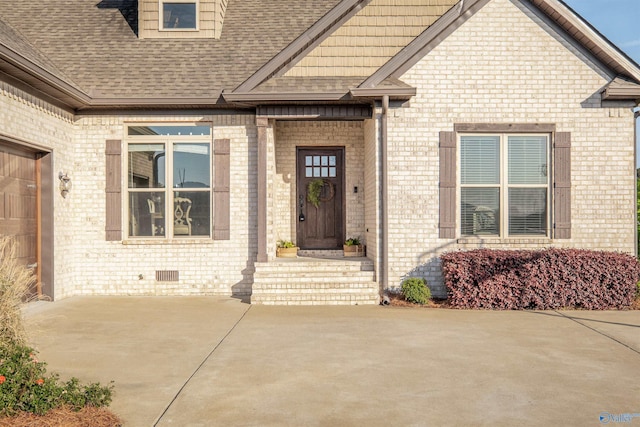view of exterior entry featuring brick siding and roof with shingles