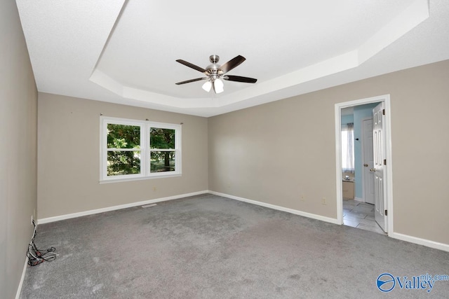 carpeted spare room featuring ceiling fan and a raised ceiling