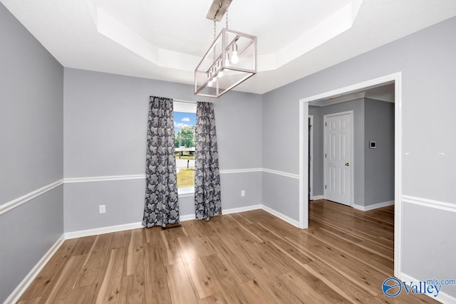 empty room featuring a raised ceiling, an inviting chandelier, and hardwood / wood-style flooring