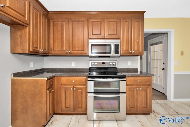 kitchen with stainless steel appliances, light tile patterned flooring, and dark stone counters