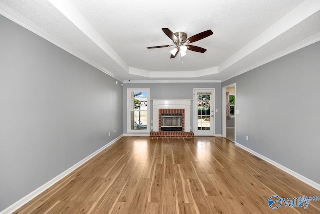 unfurnished living room with ceiling fan, a raised ceiling, light hardwood / wood-style flooring, a brick fireplace, and crown molding