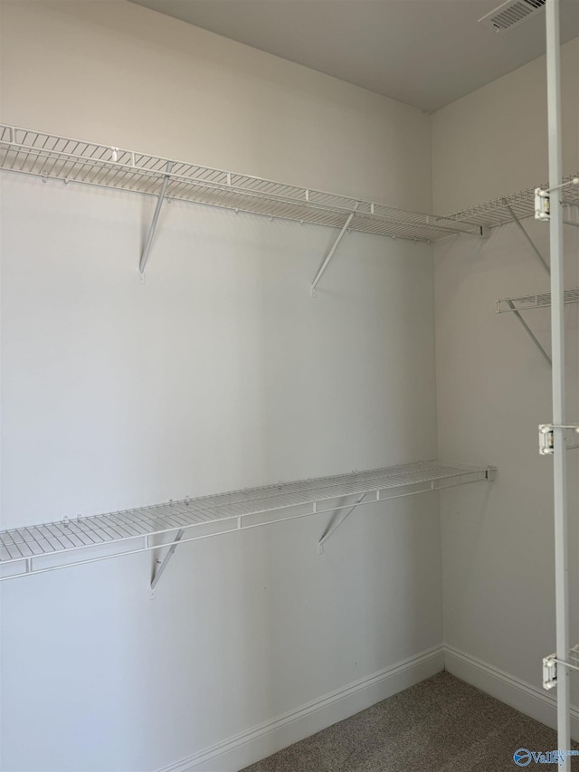 spacious closet with visible vents and dark colored carpet